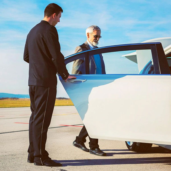 Driver helping senior adult into limousine at airport